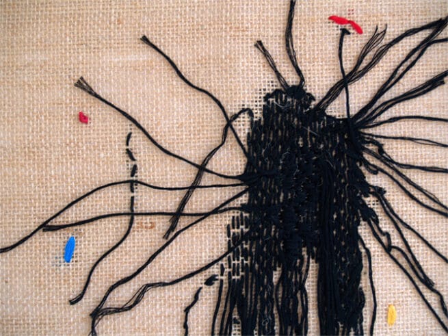 Fuegos I. Close up de la tela de arpillera y el bordado en negro con puntos de color azul, rojo, amarillo y fucsia