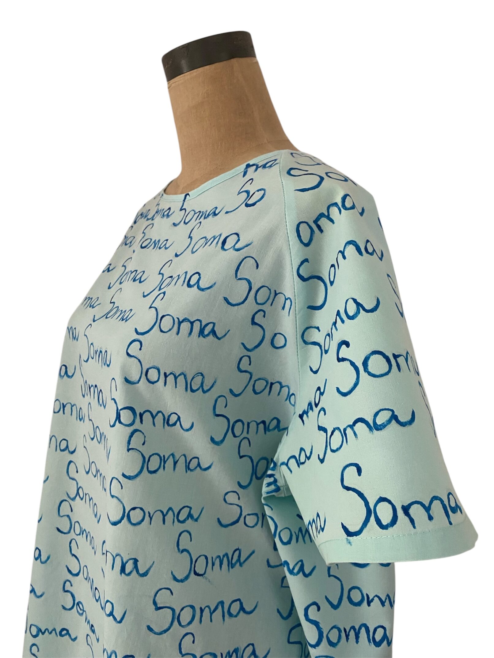 Bata de hospital tela verde clara repetición de la plabra Soma, vista de perfil medio cuerpo