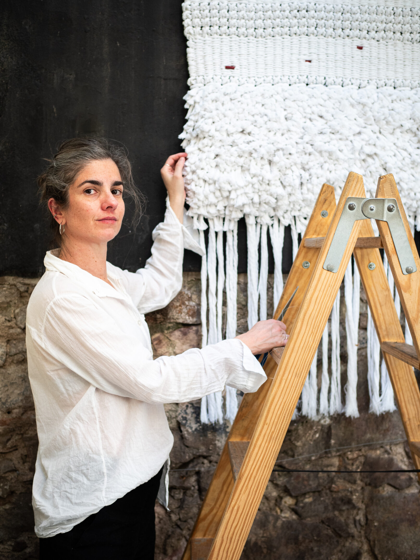 Artista textil junto al tapiz Saturación, cuerdas de algodón blancas sobre pared negra